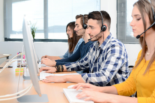 group of young people telephone operator with headset working on desktop computer in row in customer service call support helpline business center