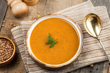 Soup made of lentil and vegetables in a rustic bowl on a canvas tablecloth. Delicious healthy vegetarian food on an old wooden table. Top view.