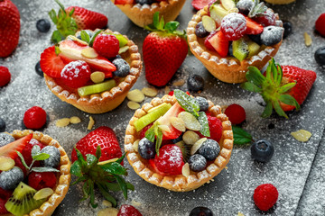 Berry tartlets with blueberries, raspberries, kiwi, strawberries, almond flakes in icing sugar.