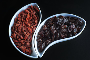 Dried goji berries and dark grapes in white bowls on a black background