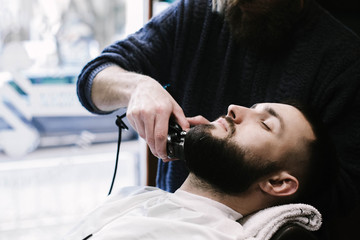 Fototapeta premium Man lies in the chair while barber cuts his beard