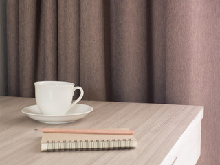 A cup of coffee and notebook on wood table . Coffee break in morning ,break working  / selective focus.Blank seating  indoor in living room .copy space for create idea for business.