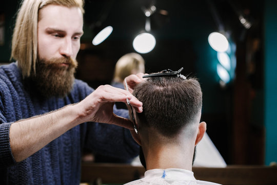 Blond barber cuts man's hair with scissors