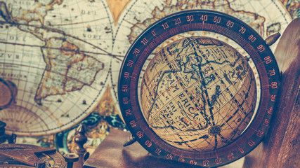 Antique bronze compass and globe sphere models on the ancient world map in vintage style picture.