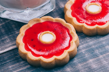 Macro shot of a cookie with red cherry jelly. Nearby is a glass of milk. Sweet food