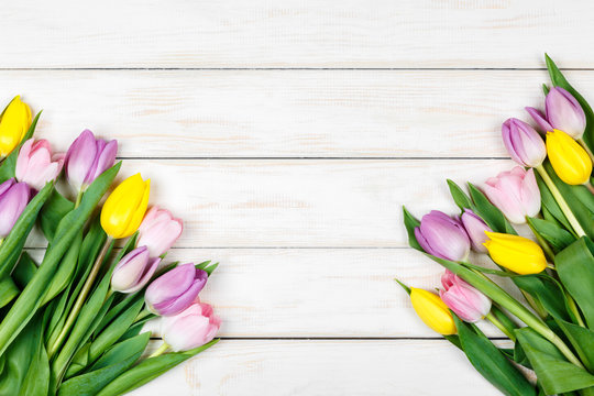 Bunch of pink and yellow tulips on a white wooden background
