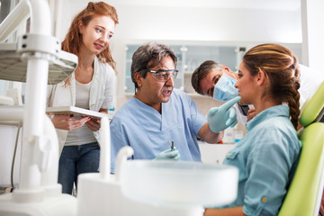 A young woman, seated in the dentist's chair, prepares herself for treatment, her trust in capable hands. Meanwhile, a two dentists discusses her care to ensure a seamless and comfortable experience.