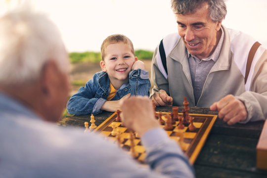 Active retired people, old friends and free time, two senior men having fun and playing chess at park, spend time with grandson