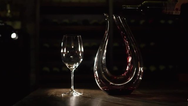 The horizontal composition of the hand pouring the red wine into the decanter placed ner the glass wine on the table.