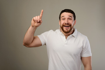 Young man has idea, pointing with finger up isolated on gray background.