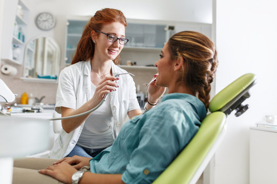 Red hair female dentist in dental office talking with female patient and preparing for treatment.