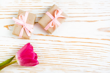 Пара упакованных подарков с розовой лентой и тюльпан на белом деревянном фоне - obrazy, fototapety, plakaty