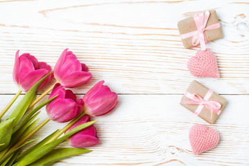 Букет тюльпанов, упакованные подарки и вязанные сердца на белом деревянном фоне