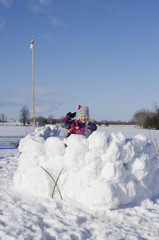 Girl standing in large snow fort with snowball