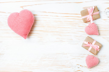 Подарки, перевязанные розовой лентой и вязанные сердца на белом деревянном фоне