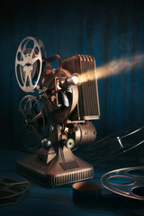vintage 8mm movie projector with 35mm reels and film on a wooden background with dramatic lighting © fergregory