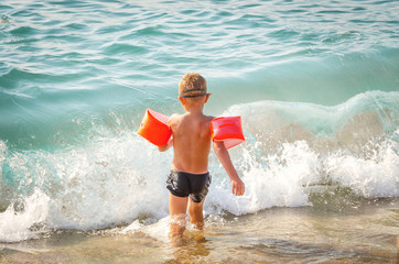 The child runs in the sea to bathe with protective inflatable sleeves