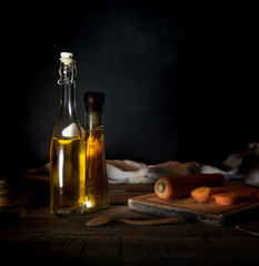 Bottles with oil, herbs and spices at wooden table on black background.
