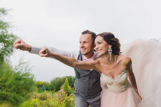 Newlyweds in a superman pose on a green lawn background, park. Average plan.