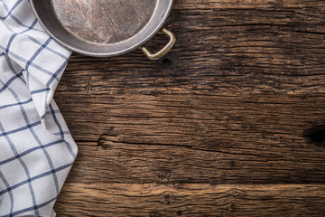 Top view of checkered tablecloth or napkin on empty wooden table.Metal old retro empty pan on oak  kitchen table. Top view.