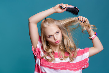 young attractive blond woman brushing her hair with pink comb on blue background