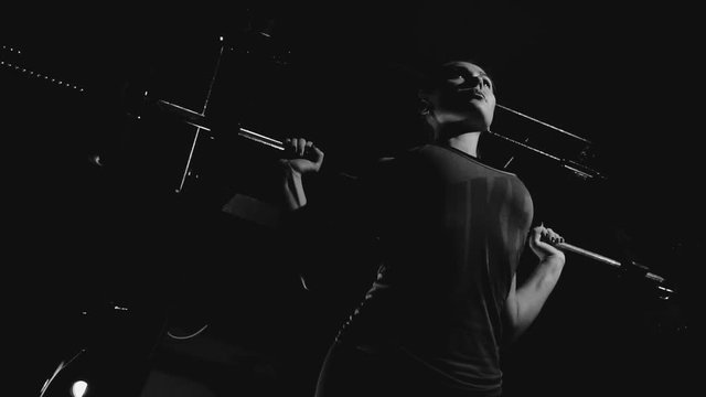 Black-and-white shot of beautiful fit sportswoman preparing to do barbell deadlift exercise