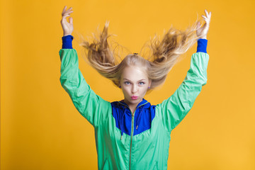 portrait of beautiful blond woman in sunglasses and blue green jacket on yellow background. hipster...