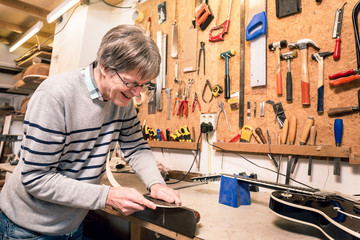 Smiling musical instrument maker working on a guitar