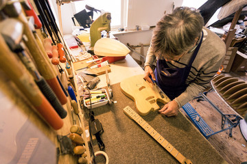 Guitar repairer clearing the sawdust from an electric guitar