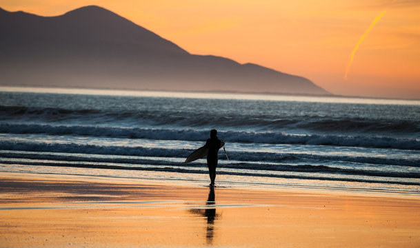 Silhouette of Surfer with surfboard walking out of the ocean at sunset 