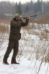 Fototapeta premium Hunter man with shotgun dressed in dark khaki clothing in the forest