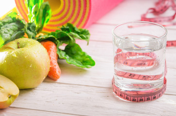 Yoga mat, water fruits and vegetables on a wooden background.