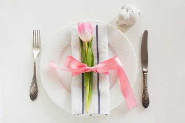 Elegance table setting with pink ribbon and tulip on white background. Easter romantic dinner. Top view.