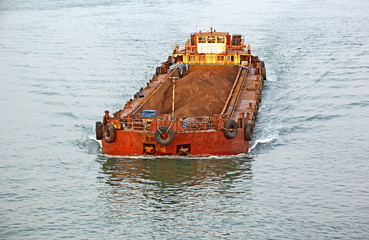 Large cargo barge transporting iron ore mined in hinterland to the main harbor for loading into big...