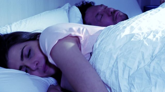 Woman cheating on sleeping husband chatting with lover on cell phone at night