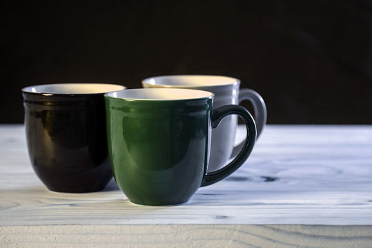 Green, black and gray mugs on plain wooden table.