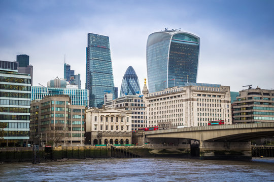 London, England - Iconic red double-decker buses on London Bridge with office buildings and famous skyscrapers at background