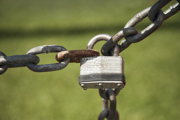 An old padlock linking two rusty chains on an out of focus green grass field