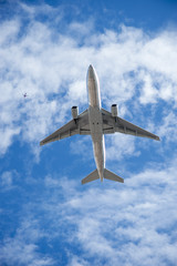 Two commercial aircraft from below, one large, one tiny on a cloudy blue sky