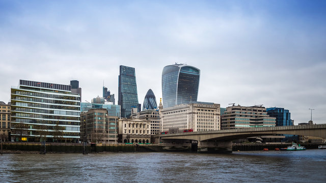 London, England - Iconic red double-decker buses on London Bridge with office buildings and famous skyscrapers at background