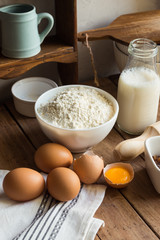 Obraz na płótnie Canvas Baking ingredients flour, eggs, open yolk, milk, rolling pin, cupboard, rustic kitchen interior, utensils, dishware