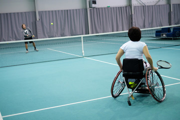 Disabled mature woman on wheelchair playing tennis with a coach