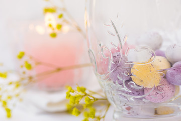 Easter table setting, details, chocolate eggs in elegant glass, candle, flowers, white background, styled