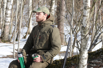 Hunter man is having rest and drinking tea in the forest