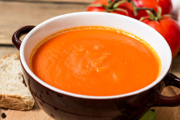 Tomato soup in ceramic bowl on wooden background.