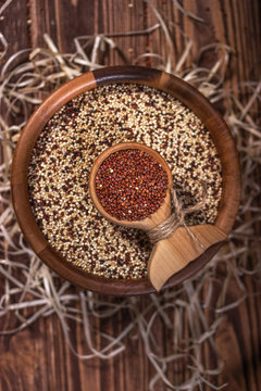 Mixed and red raw quinoa seeds in wooden bowl on a brown background. Top view.