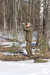 Hunter man with shotgun dressed in dark khaki clothing in the forest