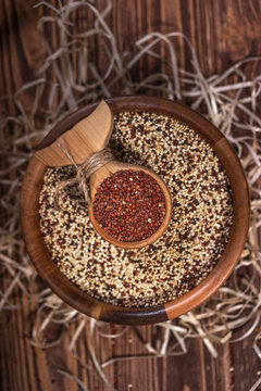 Mixed and red raw quinoa seeds in wooden bowl on a brown background