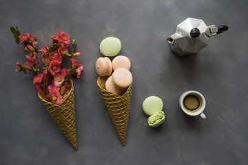 Coffee, macarons and flowers in ice cream cone on cement background