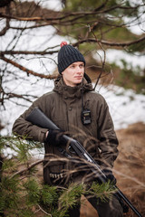 male hunter with binoculars ready to hunt, holding gun and walking in forest.